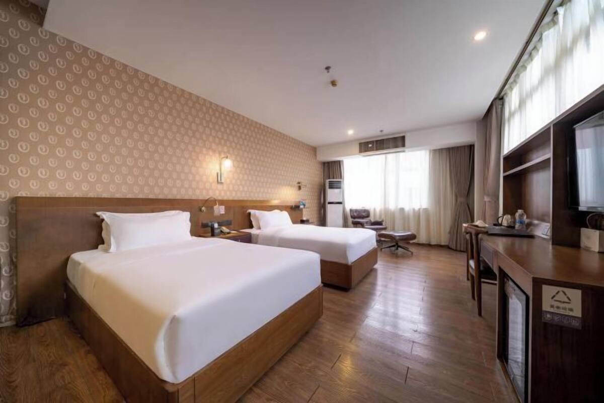 A hotel room with two beds, a desk, a chair, a TV, and a window with curtains.