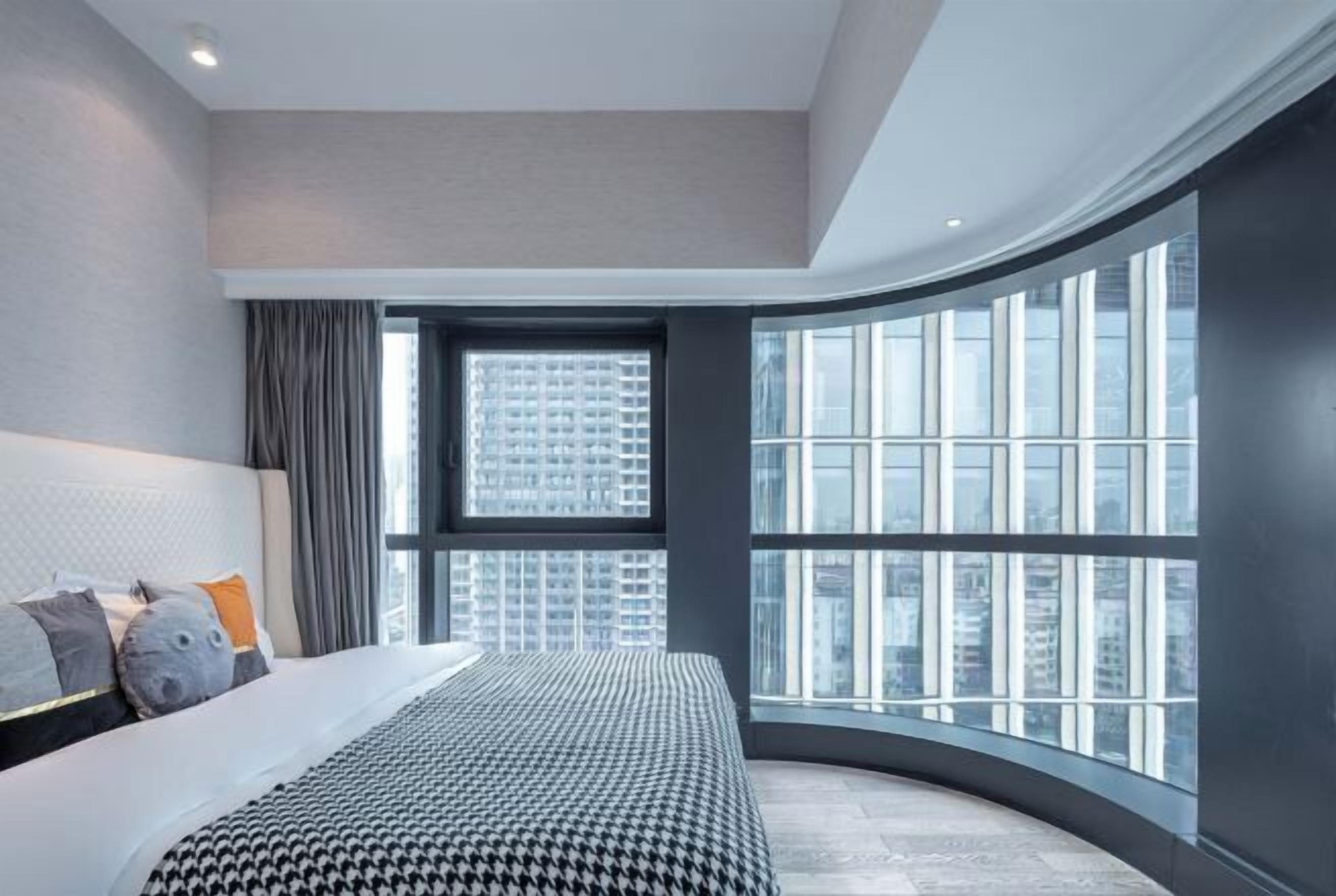 A modern bedroom with a curved window, a large bed, and a city view.