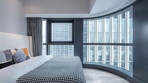 Une chambre moderne avec une fenêtre incurvée, un grand lit et une vue sur la ville.