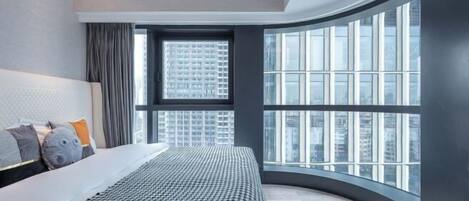 A modern bedroom with a curved window, a large bed, and a city view.