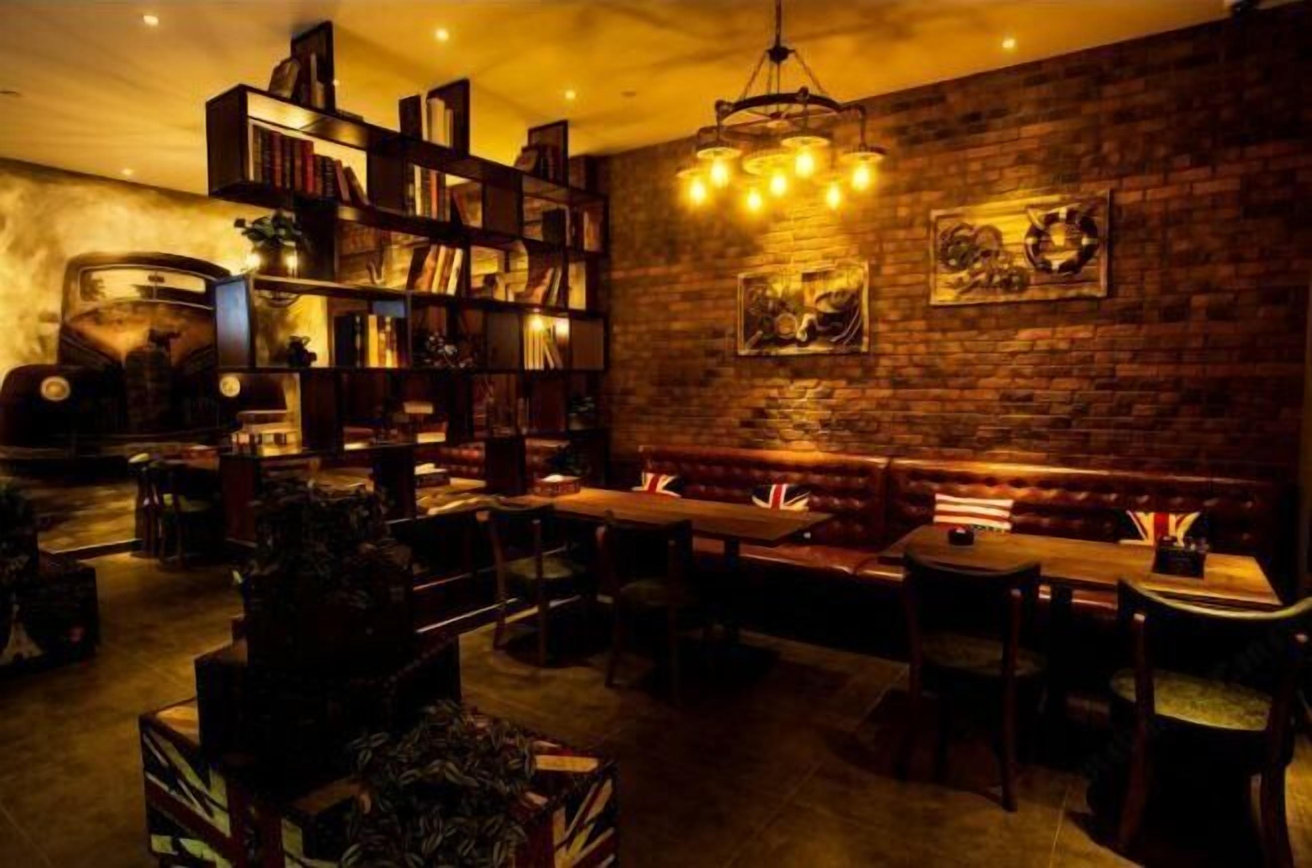 Ein gemütlicher, schummrig beleuchteter Lounge-Bereich mit Backsteinwand, Bücherregal, einer Bank und einem Tisch mit Stühlen.