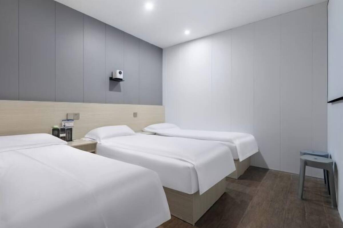 A hotel room with two beds, a small table, a chair, and a wall-mounted air purifier.