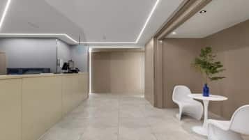 A modern hotel lobby with a reception desk, seating area, and a plant.