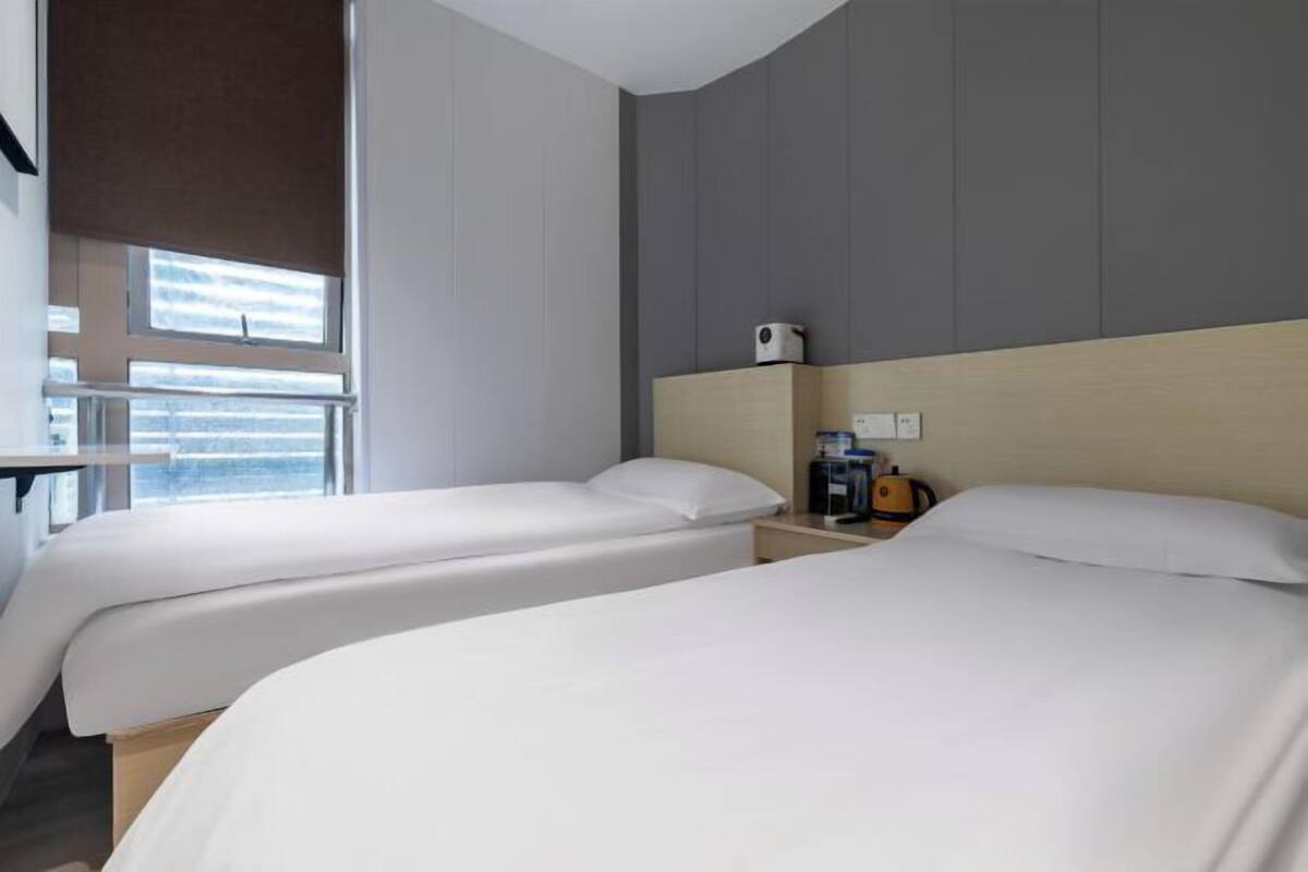 A hotel room with two beds, a nightstand with a coffee maker, and a window with blinds.