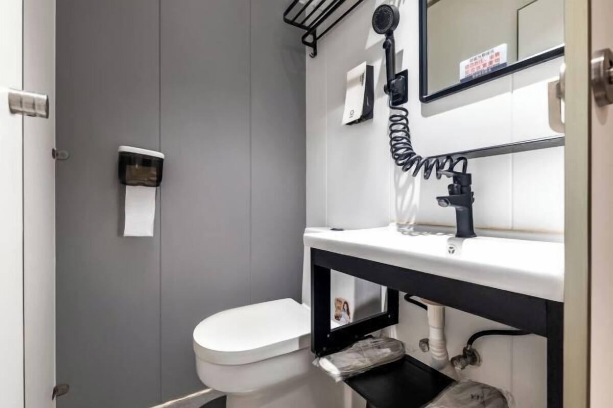 A bathroom with a white toilet, a black sink, a mirror, and a hairdryer mounted on the wall.
