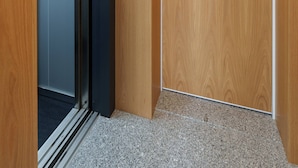A wooden door with a metal handle and a keyhole, leading to a room with a dark floor and a light switch on the wall. - VIVA Bartolomeu Beach Flats 3E (Porto)