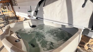 Un jacuzzi con revestimiento de piedra, estructura metálica y una zona de terraza con baldosas.