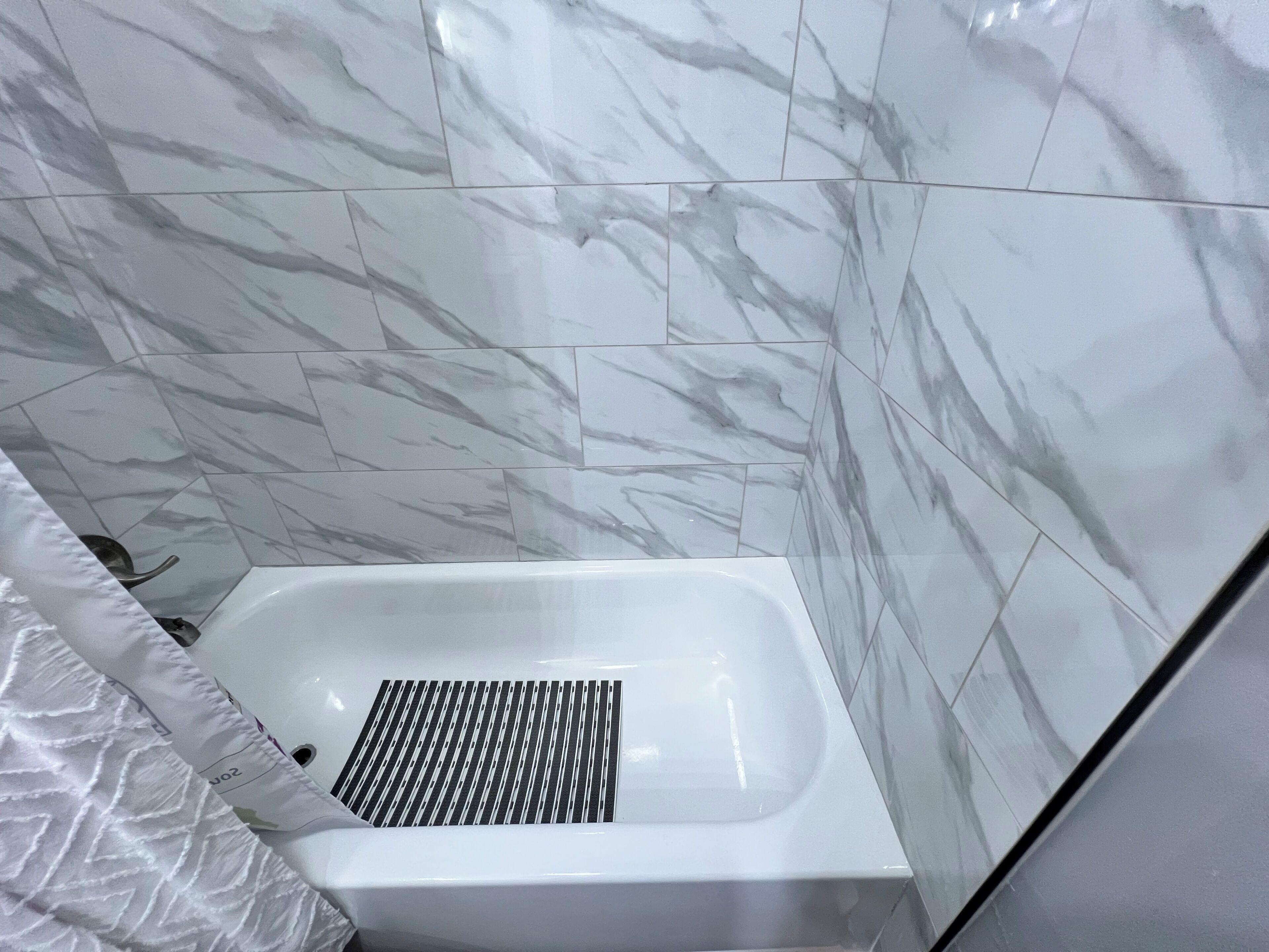 Un baño con una bañera blanca, paredes con diseño de mármol y una cortina de ducha.