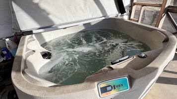 A hot tub with a control panel, located in a covered outdoor area with a concrete floor and a view of a yard.