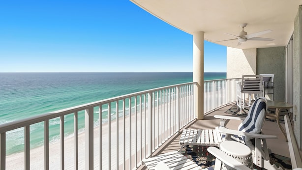 Un balcon avec vue sur l’océan, des balustrades blanches et un ventilateur de plafond.
