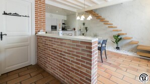 Uma cozinha moderna com parede de destaque em tijolo, porta branca e escada para uma área de jantar.