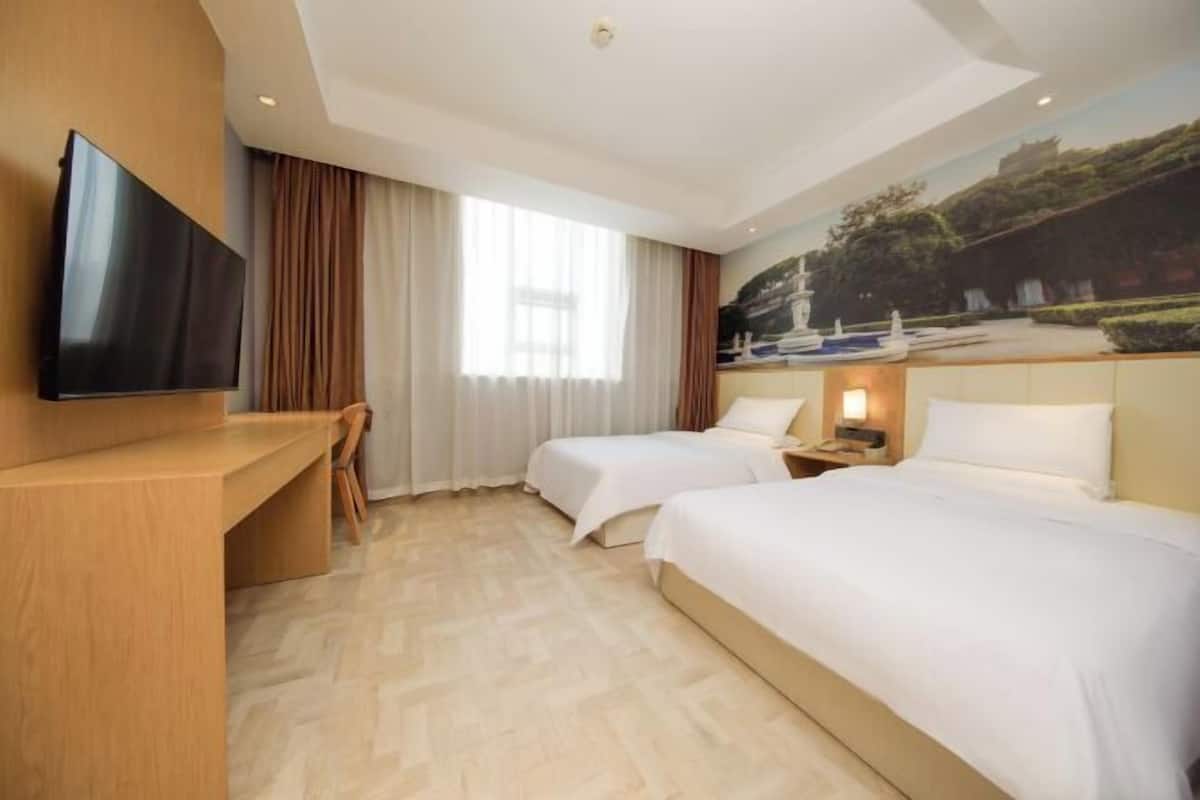 A hotel room with two beds, a desk, a TV, and a painting of a landscape.