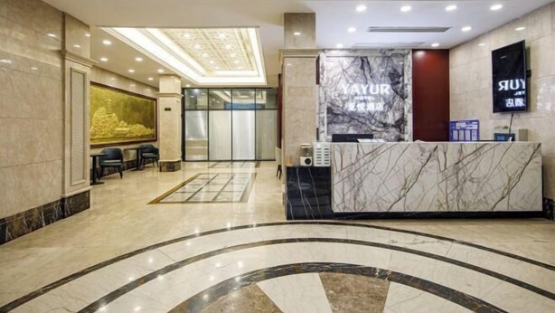 A hotel reception area with a marble reception desk, a large wall-mounted screen, and a seating area with chairs. - Yayue Hotel (Zhenjiang Railway Station North Square Xijin Ferry Store) (Zhenjiang)