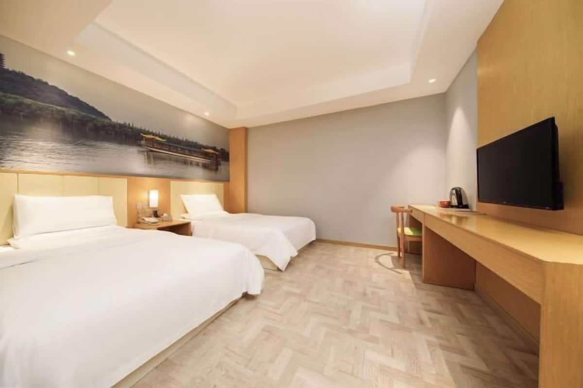 A hotel room with two beds, a wooden desk, a flat-screen TV, and a mural of a bridge over water.