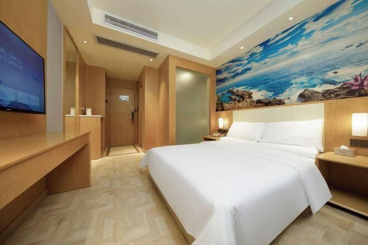 A hotel room with a bed, a TV, a nightstand, and a mural on the wall.