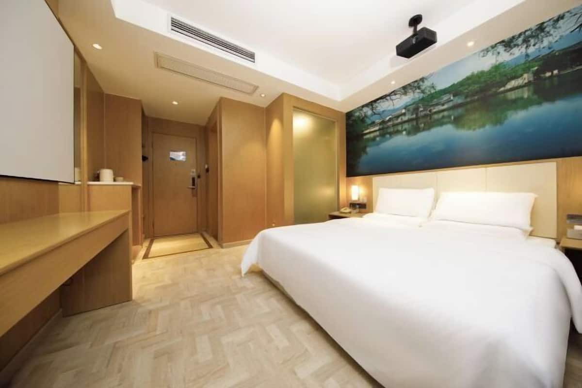 A hotel room with a bed, a desk, a wardrobe, and a painting of a landscape.