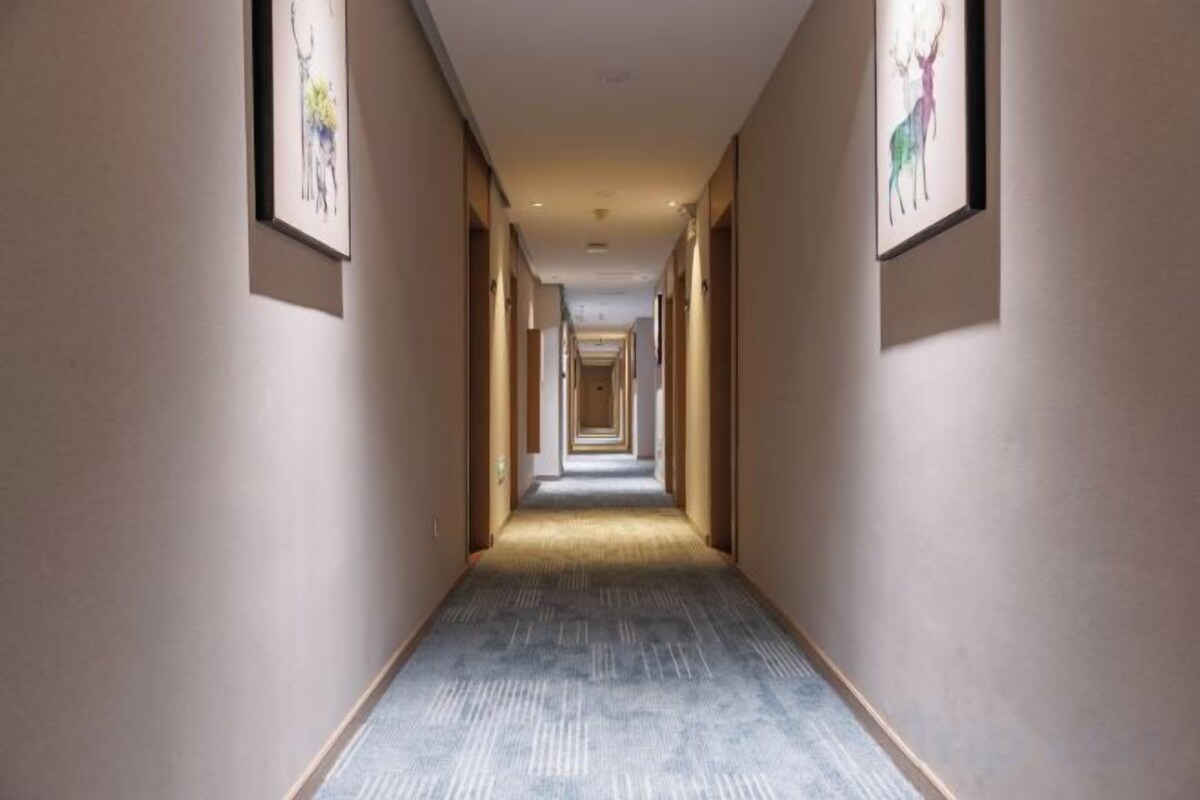 A long, narrow hotel corridor with framed artwork on the walls and a carpeted floor.