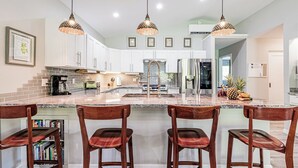 Una cocina moderna con armarios blancos, encimera de granito y tres lámparas colgantes.