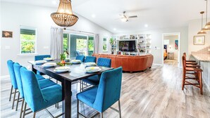 Una cocina moderna con una isla central, un comedor con sillas azules y vistas al exterior a través de grandes ventanales.