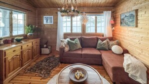 A cozy cabin interior with a brown sofa, a wooden dresser, a fur rug, and a chandelier. - 2 bedroom pet friendly home in Rendalen (Rendalen)