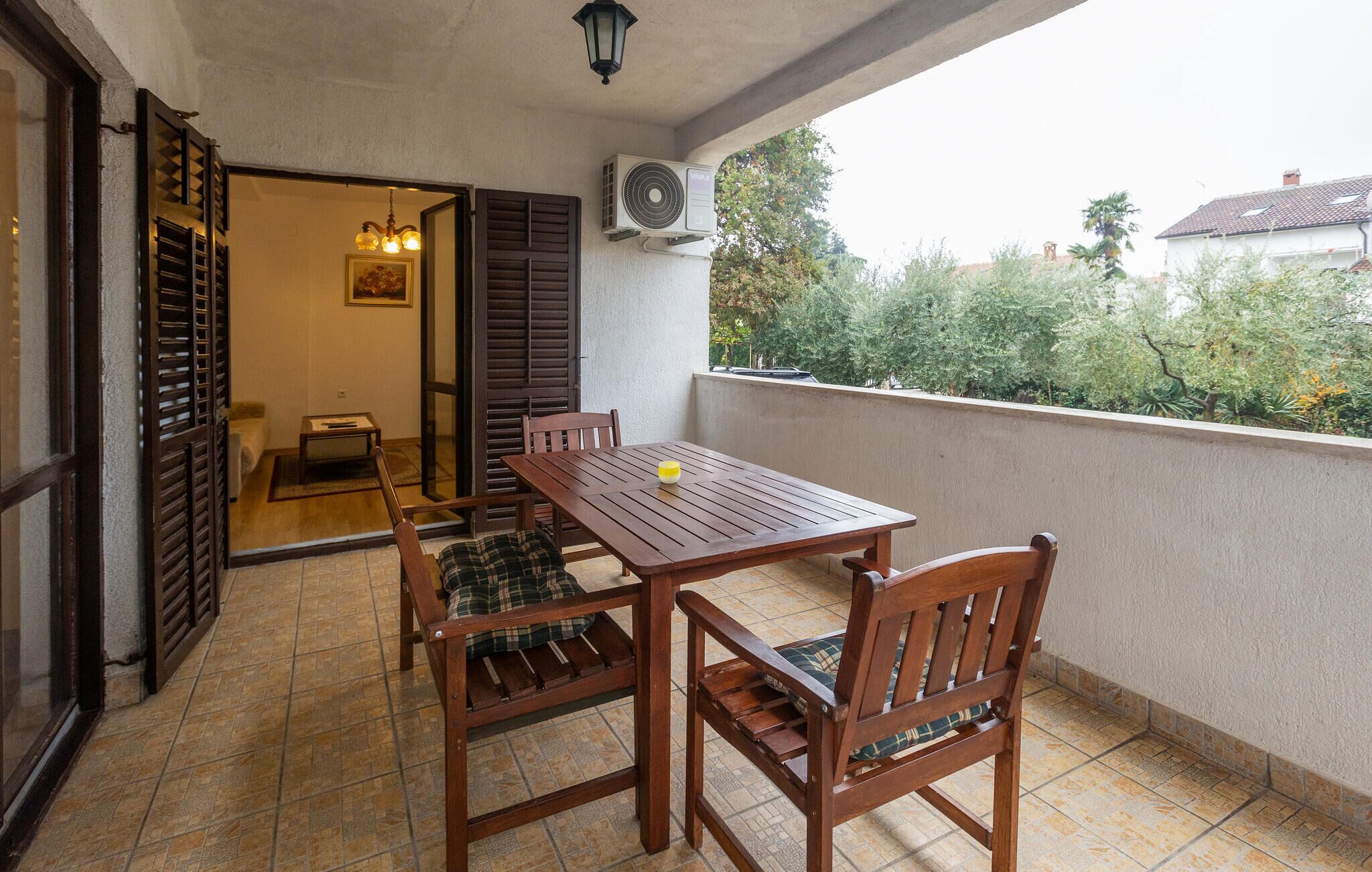 A balcony with a wooden table and chairs, a ceiling fan, and a view of greenery.