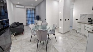 Una cocina moderna con horno empotrado, un comedor con mesa y sillas de vidrio, y un sofá gris.