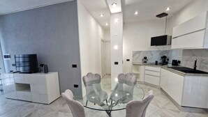 Una cocina moderna con armarios blancos, encimera de mármol y una mesa de comedor de vidrio con cuatro sillas.