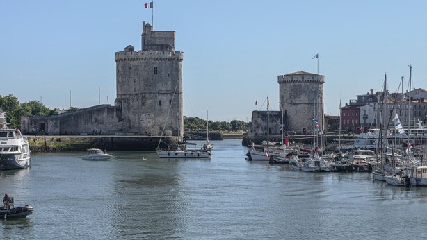 A historic waterfront with two prominent towers, a marina with various boats, and a clear sky.