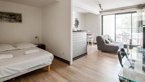 A modern hotel room with a bed, a small desk, a chair, and a large window.