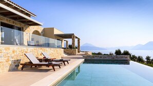 Una piscina infinita moderna con sillones de descanso y fachada de piedra.