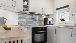Een moderne keuken met witte kasten, een inbouwoven, een koffieapparaat en een raam met bloemen.