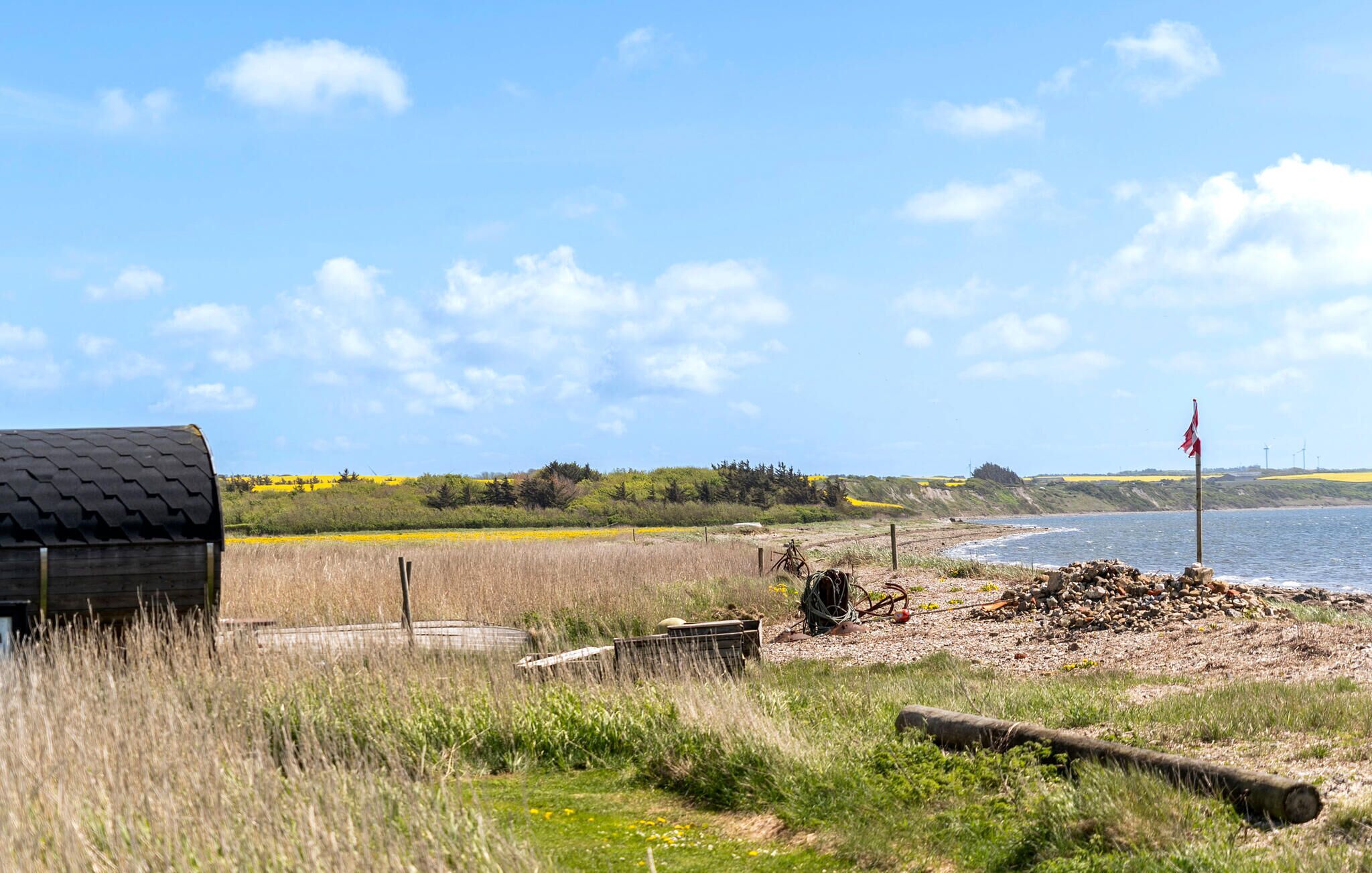A coastal landscape with a wooden structure, a pile of stones, and a flagpole by the sea.