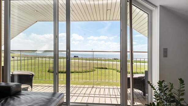 Een moderne kamer met een schuifglazen deur naar een terras met uitzicht op zee.