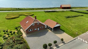 Een huis met twee verdiepingen, voorzien van een rode dakbedekking, een oprit en een verzorgd gazon.
