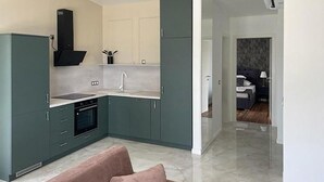 A modern kitchen with grey cabinets, a black range hood, and a built-in oven. There is a pink sofa in the foreground.