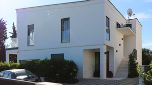 A modern two-story building with a flat roof, large windows, and a satellite dish.