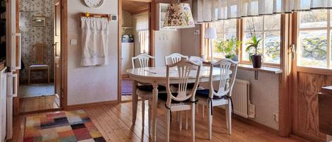 A cozy dining area with a wooden table and chairs, a colorful rug, and a window with curtains.