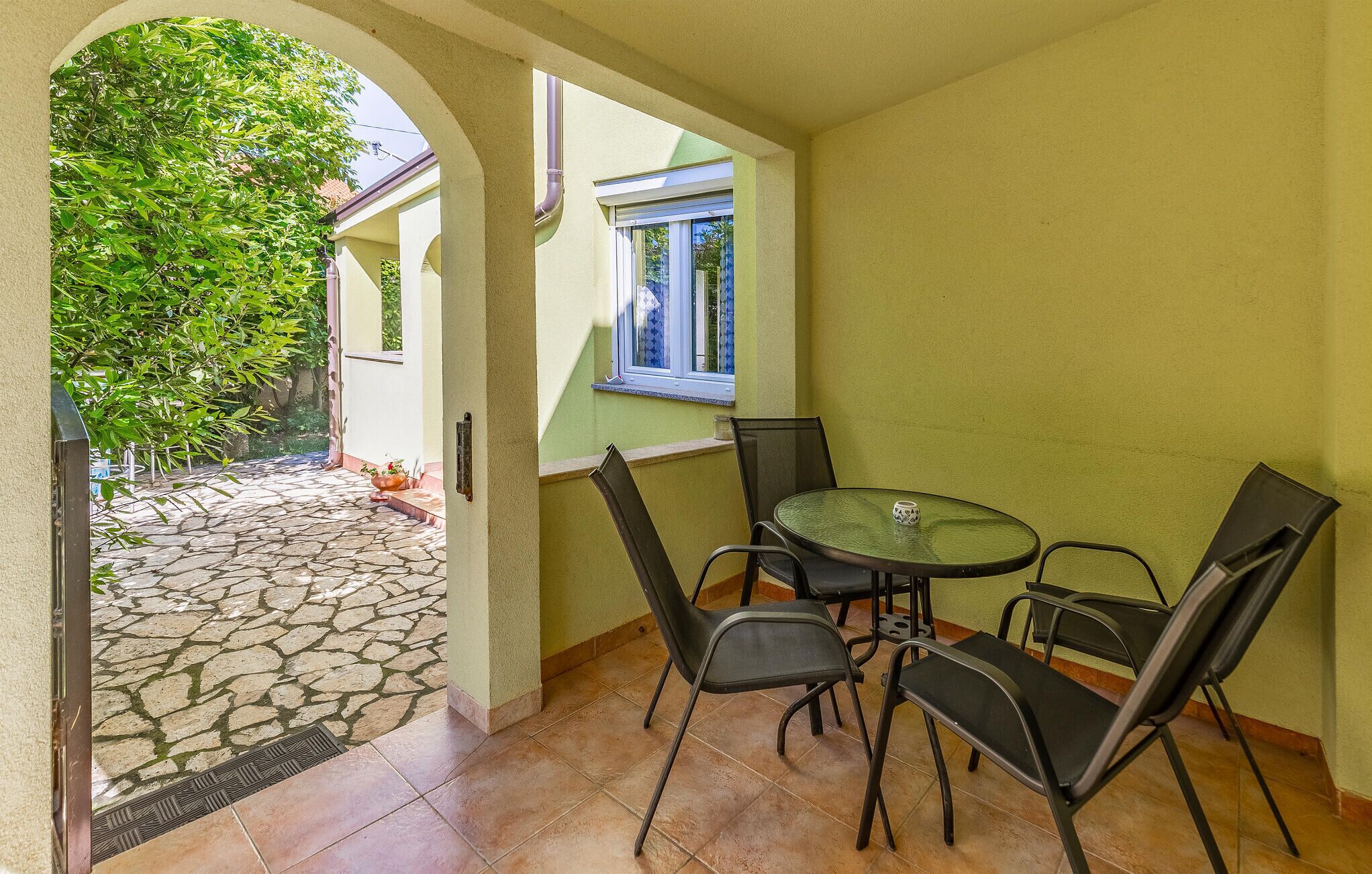 Un espace extérieur aménagé en patio, avec un sol en pierre, une table ronde et quatre chaises.