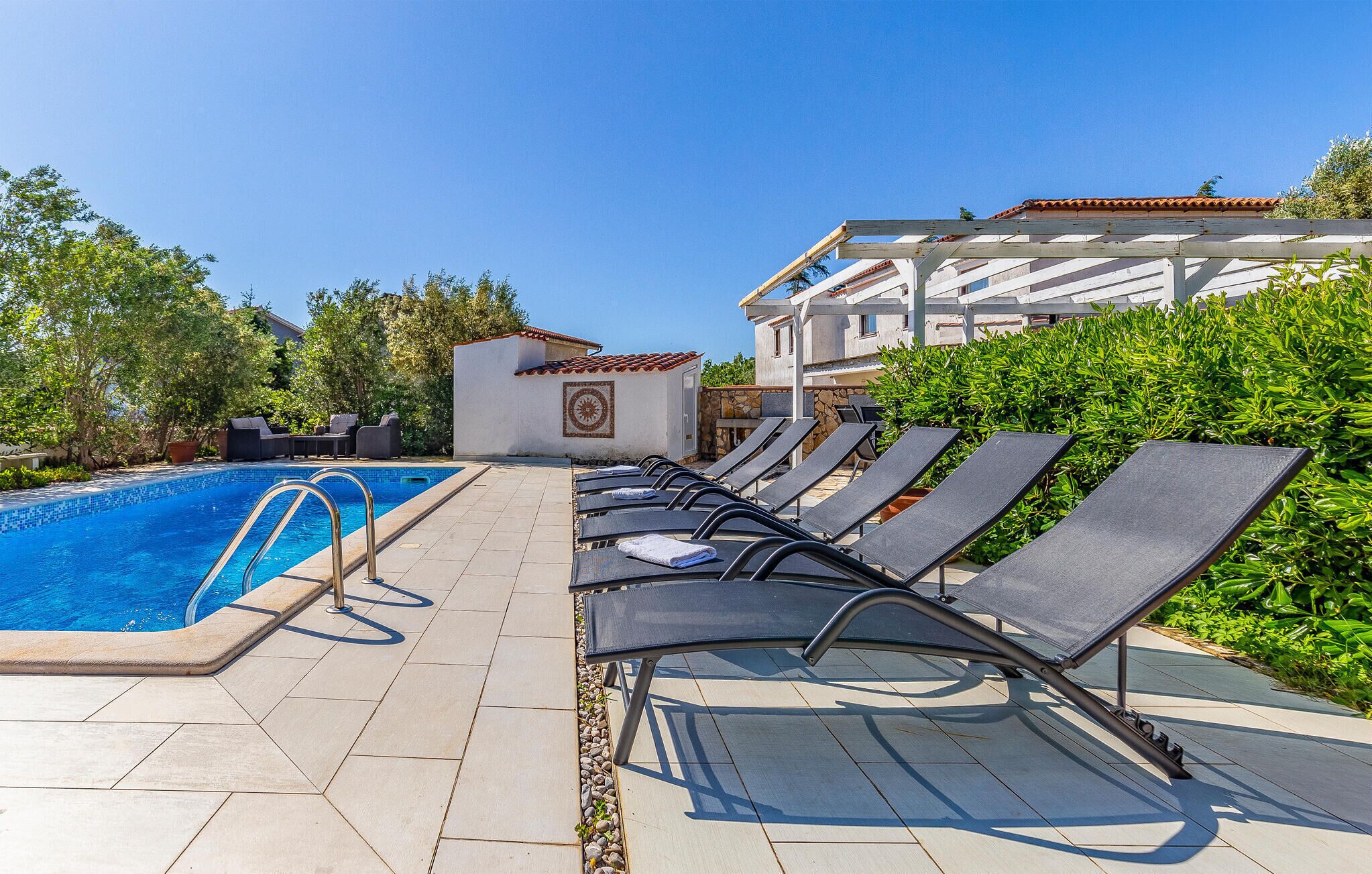 A poolside area with a swimming pool, lounge chairs, and a building with a tiled roof.