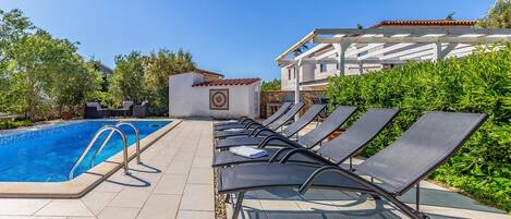 Un espace aménagé au bord de la piscine, comprenant une piscine, des chaises longues et un bâtiment doté d’un toit en tuiles.