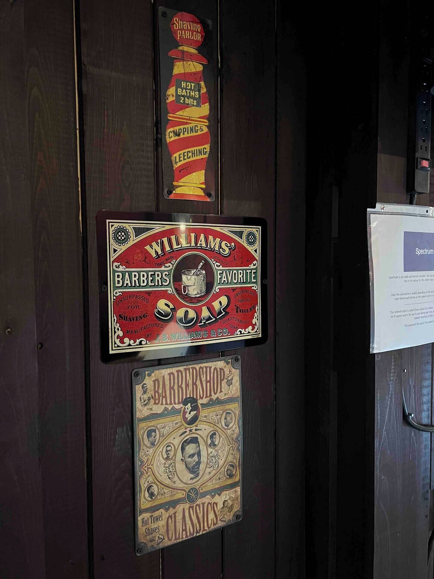 A wall with vintage barber shop signs, including 'Williams' Barbers Favorite Soap' and 'Rarborough Classics'.