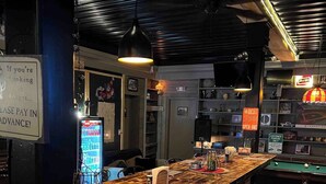 Een barruimte met een houten toog, een pooltafel en een bord waarop staat dat de bar open is.