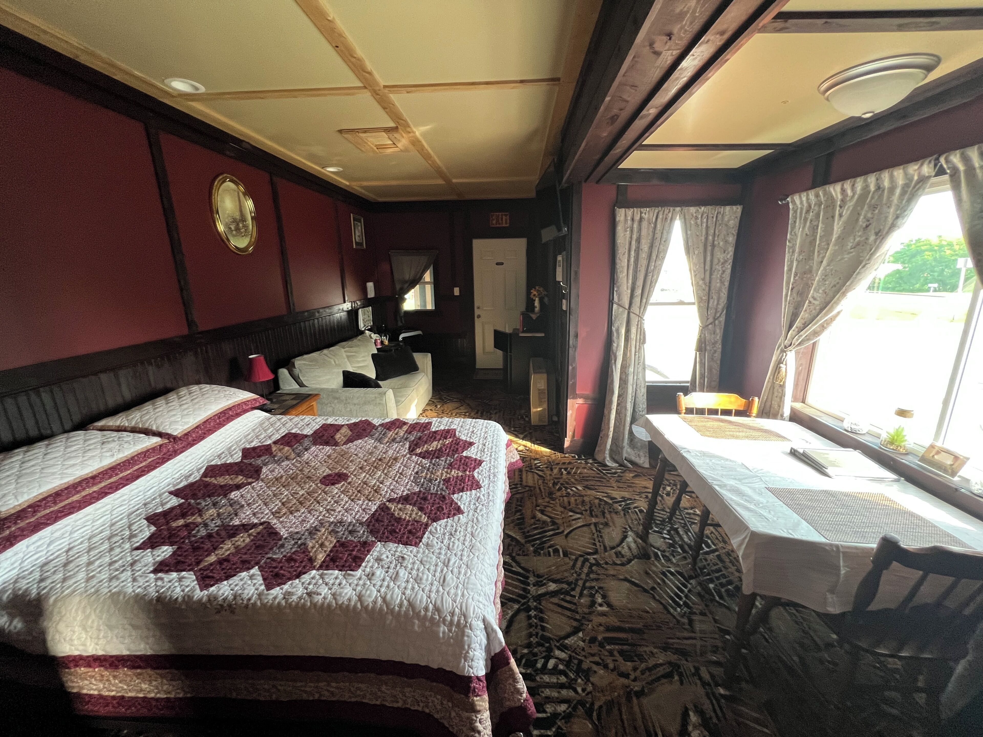 Une chambre d’hôtel avec un grand lit, une petite table, une chaise, un bureau et une fenêtre avec des rideaux.