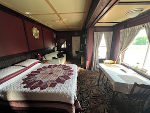 A hotel room with a large bed, a small table, a chair, a desk, and a window with curtains.
