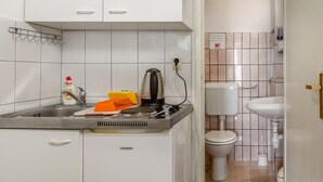 Kompakti keittiö, jossa on pesuallas, liesi ja pieni työtaso. Viereisessä kylpyhuoneessa näkyy wc.