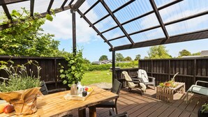 En udendørs terrasse med et træbord, stole og en pergola.