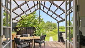 En åben terrasse med et træbord og stole, en pergola og udsigt til en have.