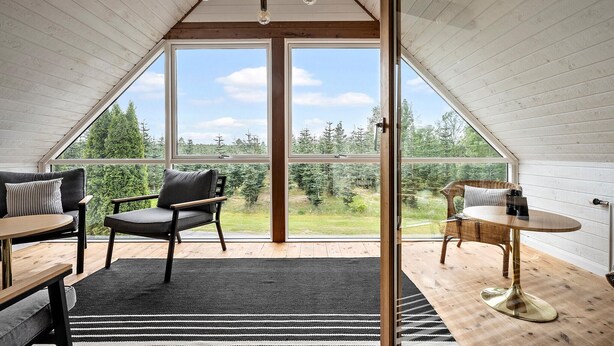 A cozy room with a large window, a sofa, a chair, a small table, and a rug.
