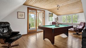 A spacious room with a pool table, leather chairs, and large windows offering a view of the outdoors.