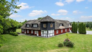 A traditional thatched-roof house with a red and white exterior, surrounded by a well-maintained lawn and trees.